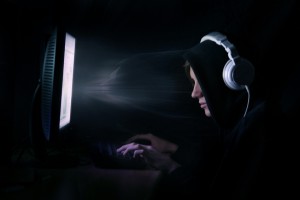 Junger Mann Sitzt mit Kopfhörern im Dunkeln vor dem Computer
